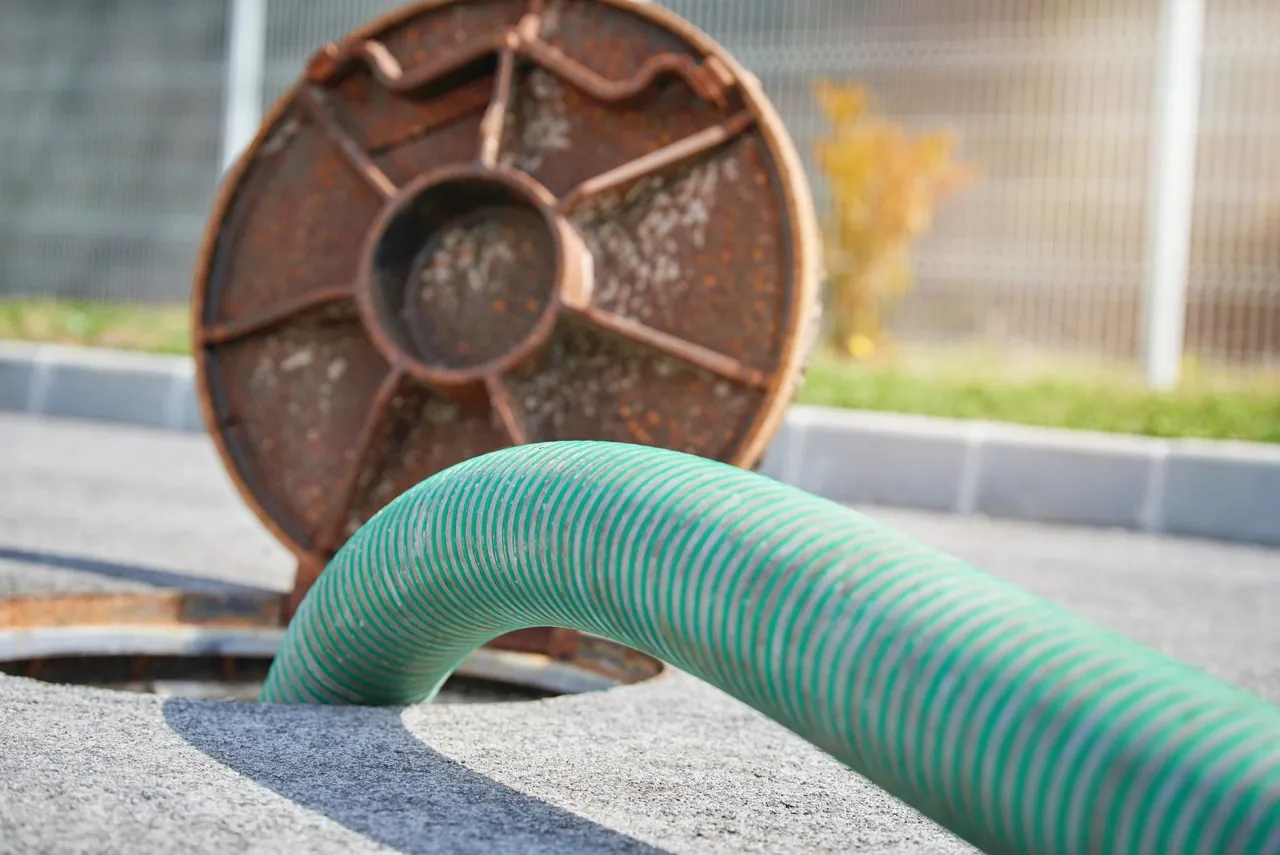 Pumping hose at an open septic system access cover